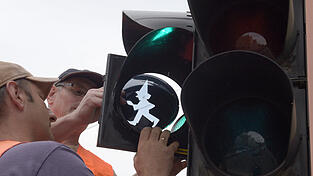 Mitarbeiter des Tiefbauamts montieren 2017 in Augsburg an einer Fußgängerampel die Silhouette des Kasperl.