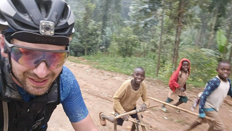 Kinder aus Ruanda mit einem selbst gebauten Rad aus Holz begleiten ihn. Kinder aus Ruanda mit einem selbst gebauten Rad aus Holz begleiten ihn.
