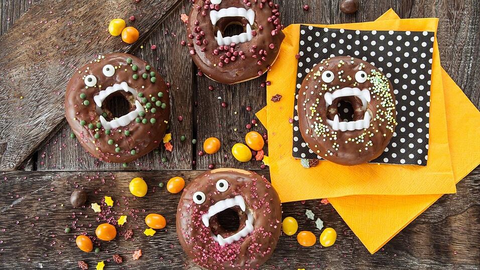 Aus einfachen Donuts werden Vampir-Donuts mit Schokolade und bunten Zuckerstreuseln. Diese kleinen Gebisse gibt es zum Beispiel im Drogeriemarkt oder in Spielzeugläden.