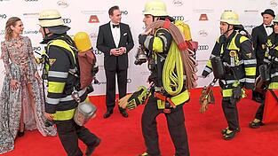 Nanu, sind das Stuntmen? Unter den &uuml;berraschten Blicken von Lisa Maria Martinek, ihrem Mann Giulio Ricciarelli und Heiner Lauterbach (r., mit Hut) laufen Feuerwehrleute beim Filmball &uuml;ber den roten Teppich vorm Bayerischen Hof. Die Feuerwehr ist wegen eines Fehlalarms gekommen.