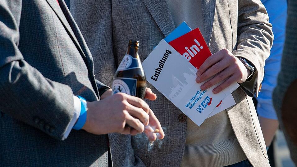 AfD-Anh&auml;nger stehen mit Stimmkarten und einer Bierflasche zusammen.