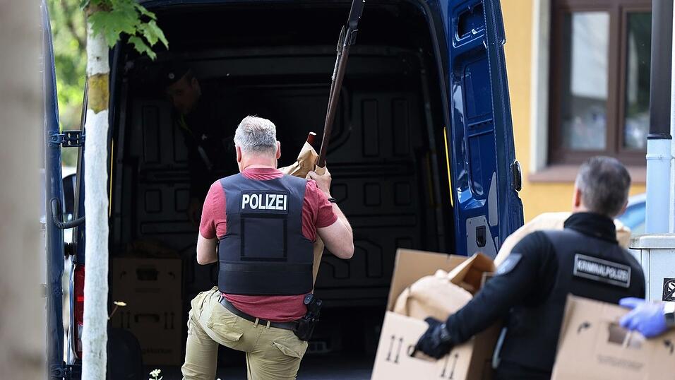 Polizisten tragen Gegenst&auml;nde, darunter mehrere Stichwaffen und Speere, aus dem Wohnhaus des Verd&auml;chtigen.