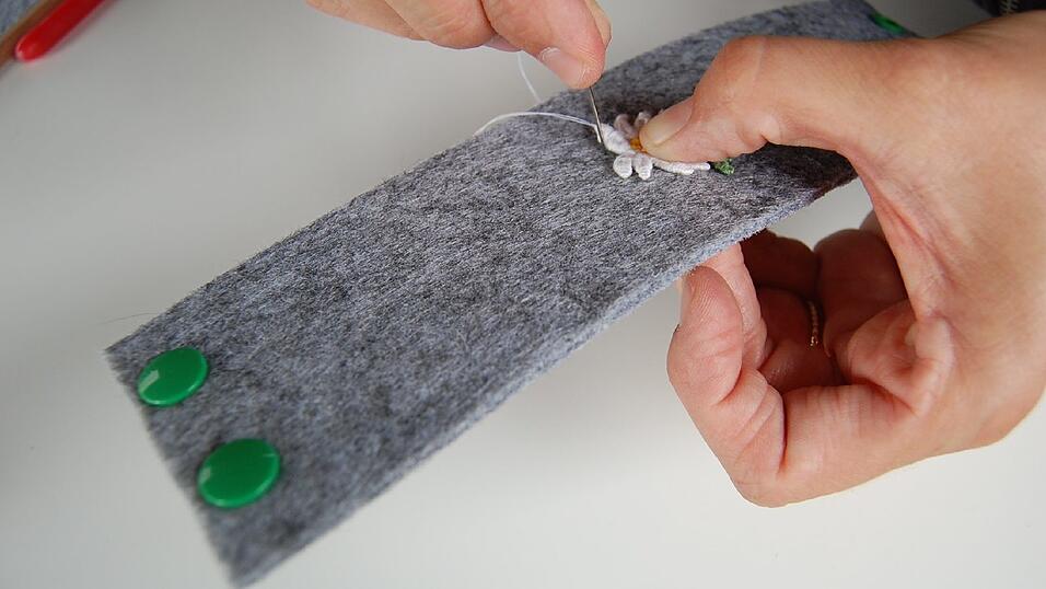 6. Jetzt noch das Edelweiß aufnähen. Benutze dafür am Besten einen Fingerhut. Filz und Aufnäher sind recht dick. Wenn du richtig fest drücken musst, saust die Nadel oft schnell in den Finger. Fang von unten an. Stich mit der Nadel durch Filz und Aufnäher und dann neben dem Aufnäher durch den Filz wieder nach unten und so weiter. Das Ganze am Rand des Aufnähers entlang bis du ganz herum bist. 6. Jetzt noch das Edelweiß aufnähen. Benutze dafür am Besten einen Fingerhut. Filz und Aufnäher sind recht dick. Wenn du richtig fest drücken musst, saust die Nadel oft schnell in den Finger. Fang von unten an. Stich mit der Nadel durch Filz und Aufnäher und dann neben dem Aufnäher durch den Filz wieder nach unten und so weiter. Das Ganze am Rand des Aufnähers entlang bis du ganz herum bist.