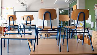 Stühle stehen in einem Klassenzimmer auf den Tischen.