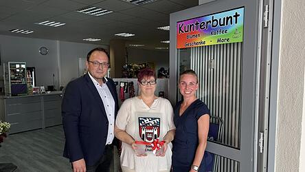 B&uuml;rgermeister Martin Stoiber und Standortkoordinatorin Theresa Buhrke (rechts) &uuml;bergeben Besitzerin Katja Geuther das Stadtwappen aus Glas.