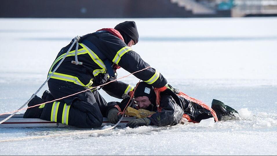 Ein Feuerwehrmann (l) rettet bei einer Übung im Stadtpark auf einem zugefrorenen See einen im Eis 'eingebrochen' Mann aus dem Wasser. Ein Feuerwehrmann (l) rettet bei einer Übung im Stadtpark auf einem zugefrorenen See einen im Eis 'eingebrochen' Mann aus dem Wasser.
