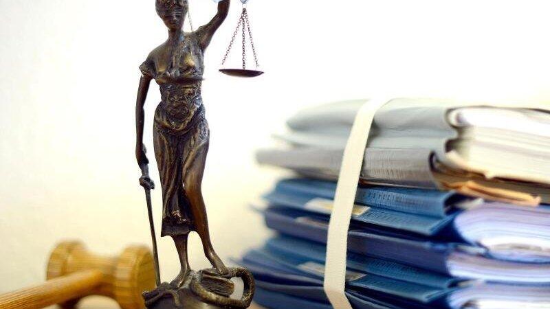 Die modellhafte Nachbildung der Justitia steht neben einem Holzhammer und einem Aktenstapel. Foto: Volker Hartmann/dpa