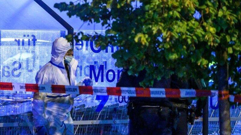 Einsatzkr&auml;fte der Polizei stehen auf einem Parkplatz neben einem Supermarkt, vor dem Sch&uuml;sse gefallen sind. Foto: Armin Weigel/dpa