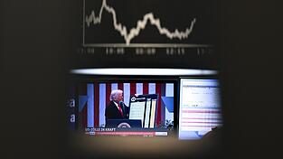 US-Präsident Trump ist auf einem Bildschirm auf dem Parkett der Frankfurter Wertpapierbörse vor der Anzeigetafel mit der Dax-Kurve zu sehen.