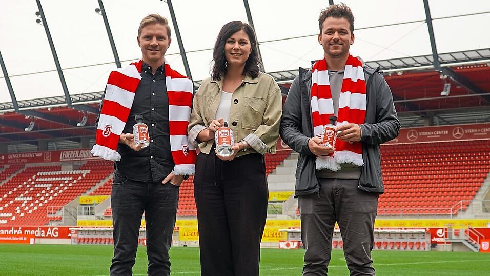 Julian Meindl, Betreiber des Caf&eacute; Malefiz (von links), Simone Piller, Leiterin Vermarktung Gesch&auml;ftskunden des SSV Jahn, und Maximilian Reif, Inhaber der Kaiser Hill 16 GmbH, pr&auml;sentieren den neuen 'Jahn Gin'.