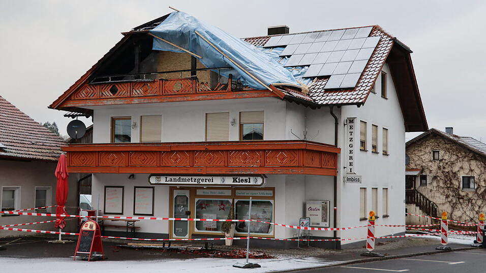 Dachziegel und verkohlte Holzreste liegen seit dem Brand vor dem Haus. Das Dach ist mit Planen geflickt. Rotes Flatterband zieht sich um das Geb&auml;ude an der Radlinger Hauptstra&szlig;e.